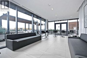 Toronto (York University Heights) condo for rent - A spacious living room with a large grey sofa and a glass wall.