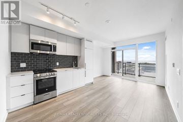 Toronto (South Parkdale) condo for rent - A modern kitchen with white cabinets and a black backsplash.