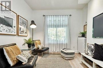 Toronto (The Beaches) multi-family for rent - A living room with a black couch, a glass table, a window with curtains, and a rug on the floor.