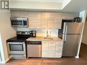 Toronto (South Parkdale) condo for rent - A kitchen with a stainless steel refrigerator, microwave, oven, and sink.