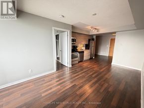 Toronto (South Parkdale) condo for rent - A room with wooden floors and a kitchen area in the background.