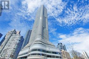 Toronto (Bay Street Corridor) condo for rent - A tall, modern building with a curved glass facade stands out against a blue sky with clouds.