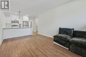 Ottawa multi-family for rent - A living room with a grey couch and a kitchen area in the background.
