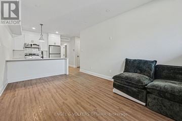 Ottawa multi-family for rent - A living room with a grey couch and a kitchen area in the background.