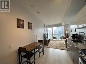 Toronto (Waterfront Communities) condo for rent - A kitchen with a table and chairs in the foreground and a balcony with a view of the city in the background.