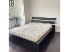 Vancouver apartment for rent - A bed with a white mattress and a black headboard is in a room with a wooden floor.