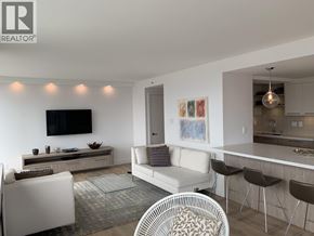 Vancouver apartment for rent - A modern living room with a white couch, a glass coffee table, and a television mounted on the wall.