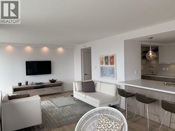 Vancouver apartment for rent - A modern living room with a white couch, a glass coffee table, and a television mounted on the wall.