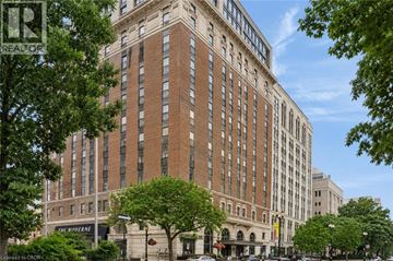 Hamilton condo for rent - A tall building with many windows is surrounded by trees.