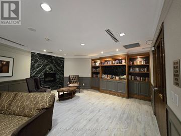 Oakville (Ro River Oaks) condo for rent - A living room with a couch, a chair, and a bookshelf filled with books.