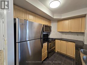 Oakville (Ro River Oaks) condo for rent - A kitchen with a stainless steel refrigerator, black stove, and wooden cabinets.