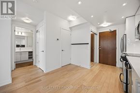 Toronto (Mimico) condo for rent - A spacious room with wooden floors and white walls, with a kitchen visible in the background.