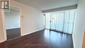 Toronto (Willowdale East) condo for rent - A room with wooden floors and white walls, with a door on the left and a window with blinds on the right.