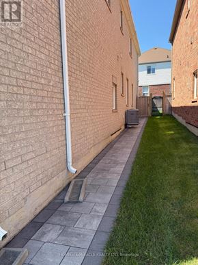 Oshawa (Taunton) apartment for rent - A narrow alley with a brick wall on one side and a grassy area on the other.