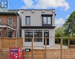 Toronto (Greenwood-Coxwell) apartment for rent - A two-story building with a grey facade and black windows is surrounded by a wooden fence.