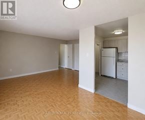 Toronto (Mount Olive-Silverstone-Jamestown) condo for rent - A room with a wooden floor and white walls, with a kitchen area visible in the background.