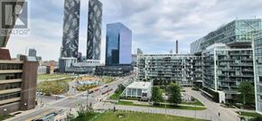 Toronto (Waterfront Communities) condo for rent - A cityscape with a mix of modern and older buildings, a road with moving vehicles, and a partly cloudy sky.