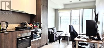 Toronto (Waterfront Communities) condo for rent - A modern kitchen with a black countertop and a living area with a couch and a TV.
