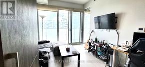 Toronto (Waterfront Communities) condo for rent - A living room with a flat screen TV mounted on the wall and a sliding glass door leading to a balcony.