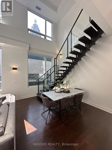 Toronto (Waterfront Communities) condo for rent - A modern living room with a glass table and chairs, a couch, and a staircase with a metal railing.