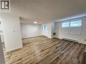 Brantford condo for rent - A spacious room with wooden flooring and white walls.