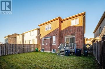 Brampton (Bram East) apartment for rent - A house with a brown brick exterior and a white window is surrounded by a wooden fence and has a green trash can in the yard.