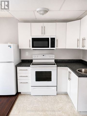 Collingwood townhouse for rent - A white kitchen with a black countertop and a white fridge.