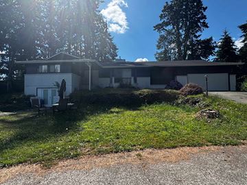 Spanaway apartment for rent - A house with a white exterior and a brown roof is surrounded by green grass and trees.
