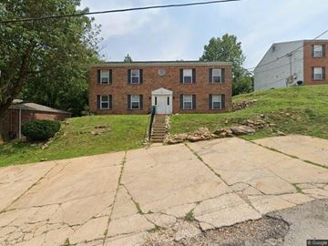 Fenton apartment for rent - A brick building with a white door and windows is surrounded by a grassy area and a cracked concrete walkway.
