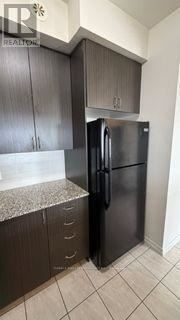 Brampton (Bram West) condo for rent - A black refrigerator is in a kitchen with dark wood cabinets.