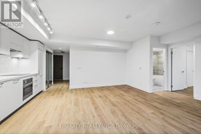 Toronto (Thorncliffe Park) condo for rent - A spacious room with wooden flooring and white walls, with a kitchen area to the left and a door to the right.