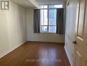 Mississauga (City Centre) condo for rent - A room with wooden flooring and a window with a view of a building.