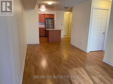 Mississauga (City Centre) condo for rent - A room with wooden floors and white walls, with a kitchen area in the background.
