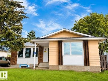 Edmonton apartment for rent - A house with a brown roof and white trim is surrounded by green grass and trees.