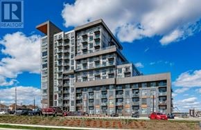 Hamilton (Waterdown) condo for rent - A modern multi-story building with a glass facade and a parking lot in front.