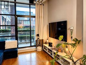 Toronto (Niagara) condo for rent - A living room with a large window, a blue couch, and a TV mounted on the wall.
