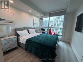 Toronto (Niagara) condo for rent - A bedroom with a bed, nightstand, and a window overlooking a cityscape.