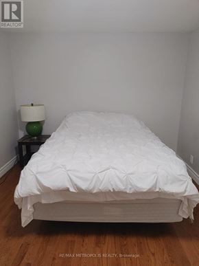 Oshawa (Lakeview) apartment for rent - A white bed with a white comforter and a white lamp with a green lampshade on a black table.
