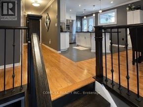 Oshawa (Centennial) apartment for rent - A staircase with a black railing leads to a living room with a kitchen in the background.