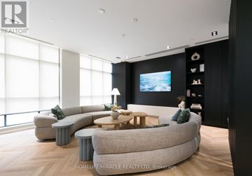 Brampton (Fletcher's Creek South) condo for rent - A modern living room with a large grey sofa and a television on the wall.