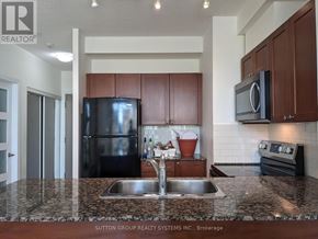 Mississauga (City Centre) condo for rent - A kitchen with a black fridge and microwave, brown cabinets, and a granite countertop.