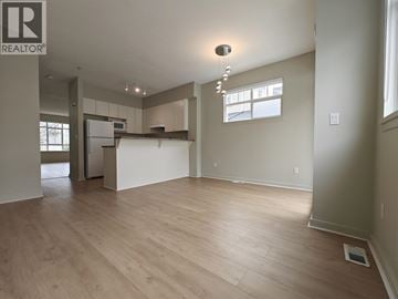 Vancouver townhouse for rent - A spacious room with wooden flooring and a kitchen area in the background.