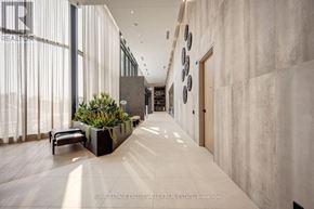 Vaughan (Steeles West Industrial) condo for rent - A long hallway with a bench and a planter on the left and a wall of circular plates on the right.