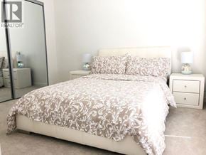 Coquitlam apartment for rent - A bed with a floral patterned comforter is in the foreground of a well-lit bedroom.