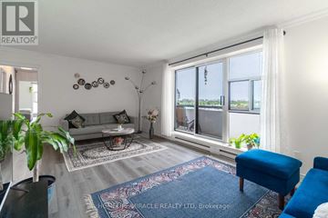 Mississauga (Applewood) condo for rent - A living room with a grey sofa, a blue ottoman, and a rug with a pattern.