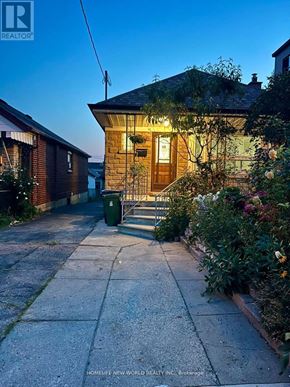 Toronto (Keelesdale-Eglinton West) apartment for rent - A house with a brown door and windows is surrounded by greenery and a sidewalk.