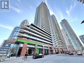 Toronto (Mimico) condo for rent - A tall building with a glass facade stands in front of a smaller building with a red brick facade.