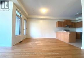 Richmond Hill townhouse for rent - A spacious room with wooden flooring and a kitchen area with brown cabinets.