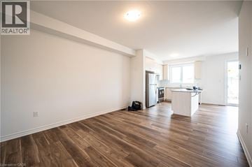 Kitchener townhouse for rent - A spacious room with wooden flooring and a kitchen area in the background.