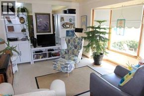Calgary apartment for rent - A living room with a grey couch, a chair with a floral pattern, a bookshelf, and a potted plant.